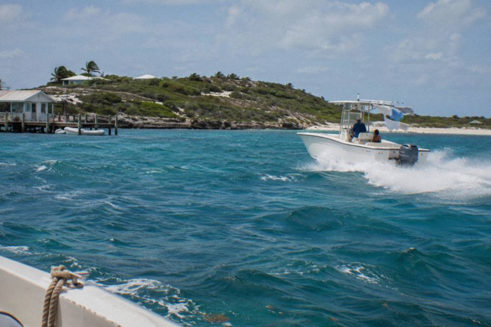 A powerboat cutting across open turquoise water toward a small Exuma cay