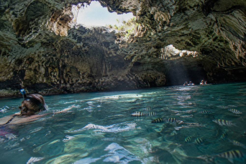 Snorkeler floating in a sunlit sea cave with fish below the surface