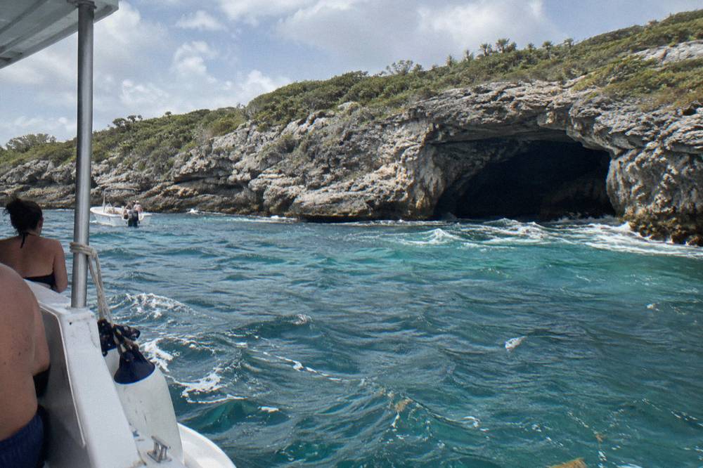Boat anchored beside a small limestone cay with a dark cave entrance at the waterline