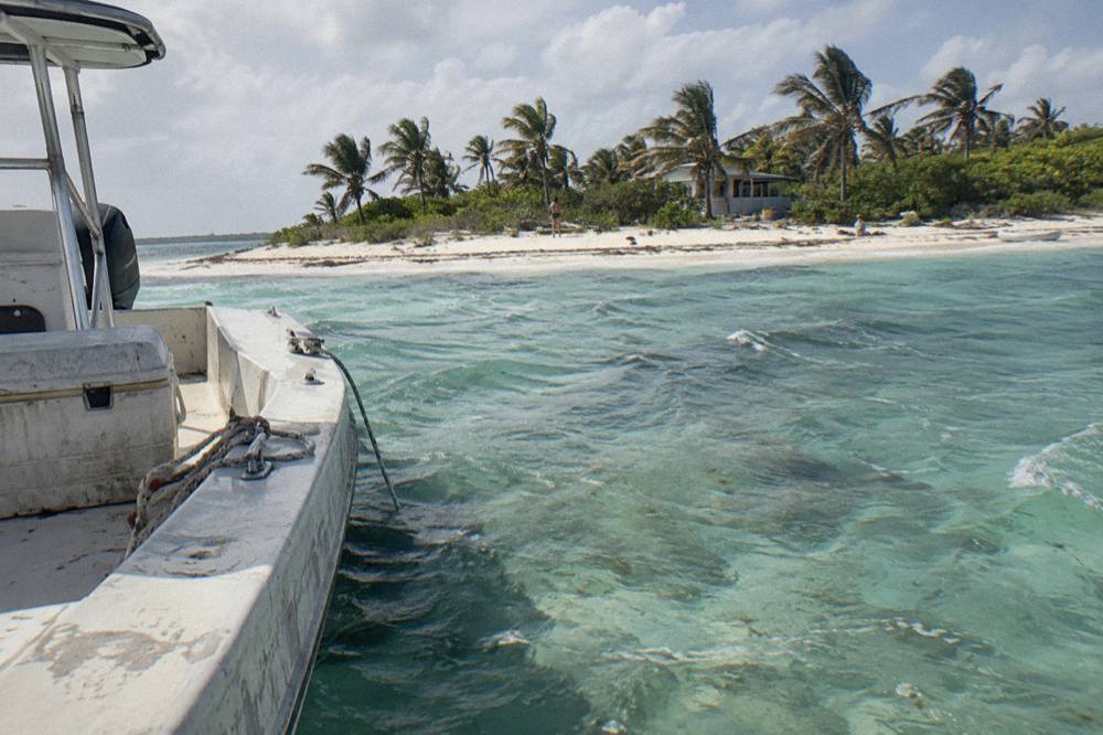 A powerboat anchored in clear shallow water beside a small sandy cay with palm vegetation