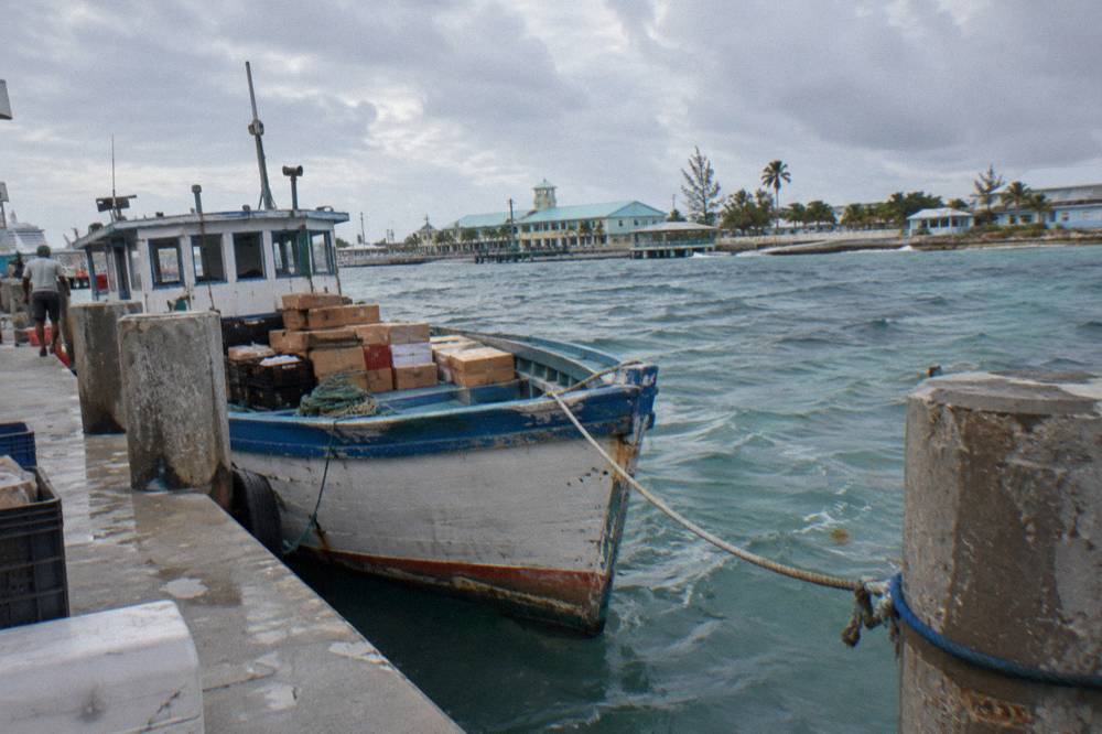 A weathered wooden mail boat tied at a dock in Nassau harbour