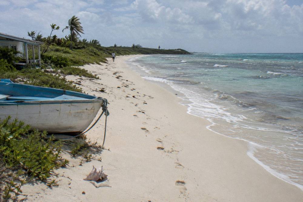 A quiet stretch of pale sand and calm clear water under a partly cloudy sky