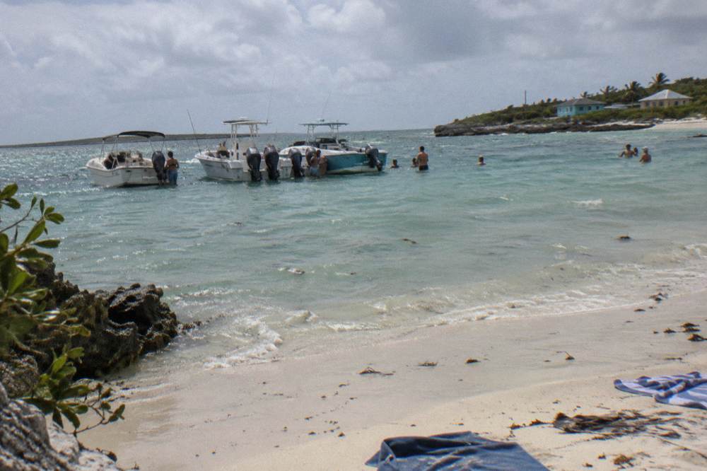 Several small boats anchored close together near a beach with visitors standing in shallow water
