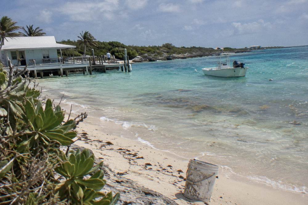 A sandy beach with clear shallow water and a small boat anchored offshore