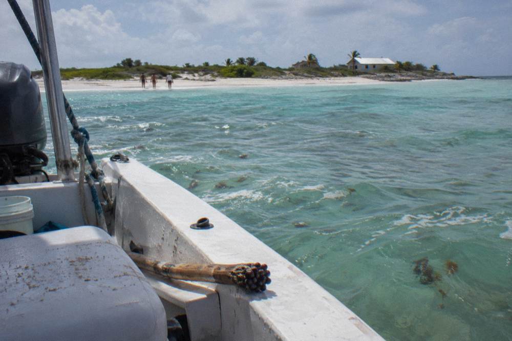 A small boat anchored beside a white sandbar ringed by shallow turquoise water