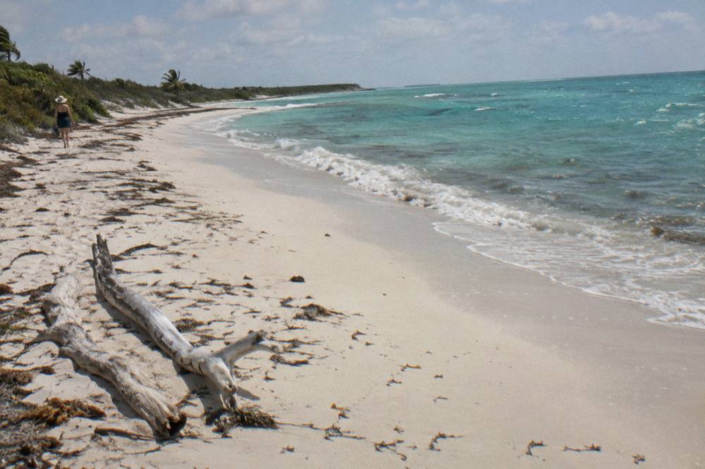 A long empty white sand beach curving beside calm turquoise water under a clear sky