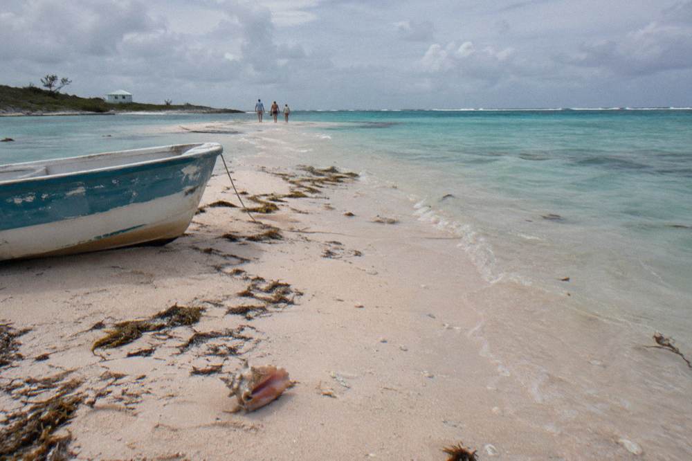 A wide sandbar emerging from glassy turquoise water under scattered clouds