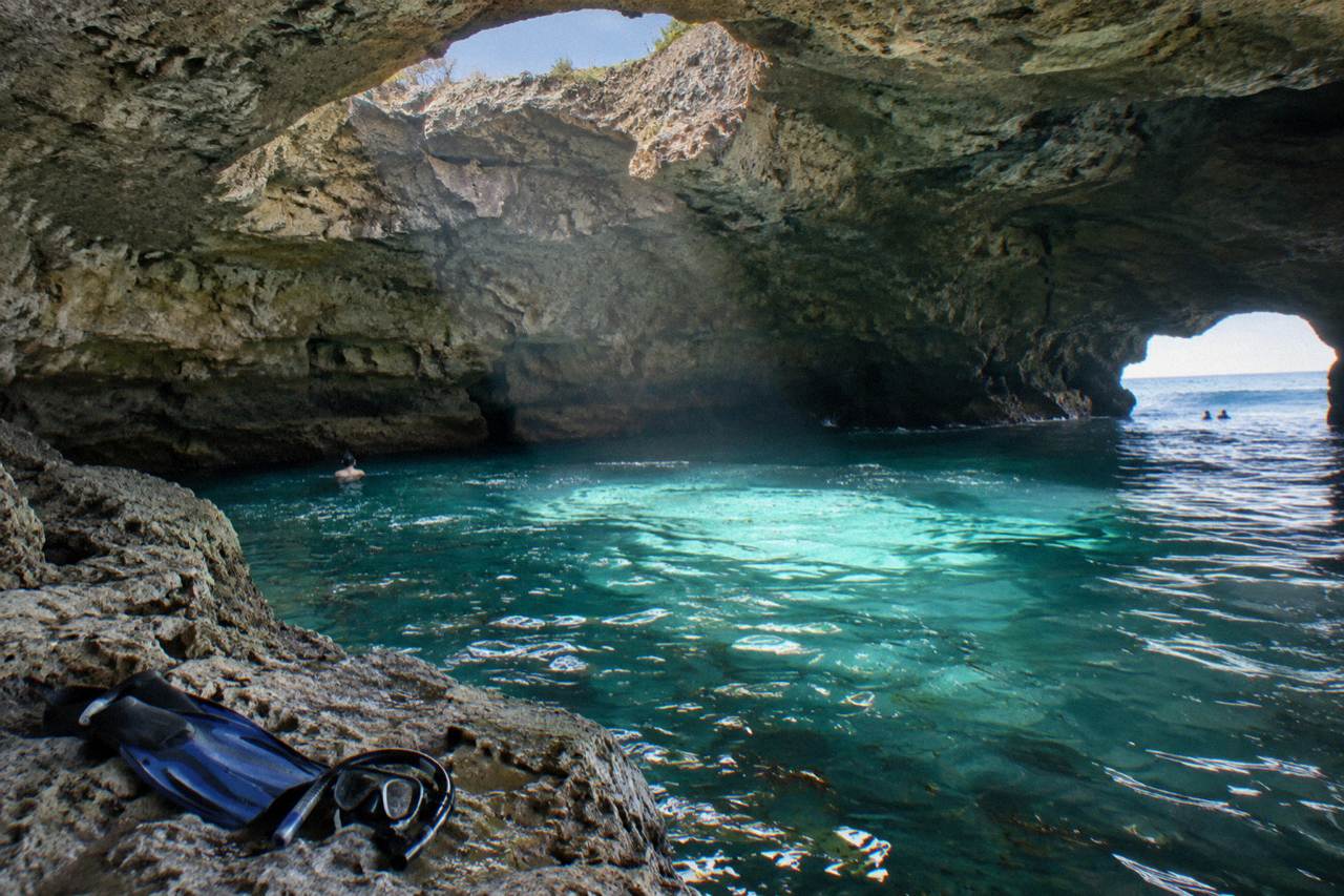 Sunlight streaming through the roof openings of a limestone sea cave onto turquoise water