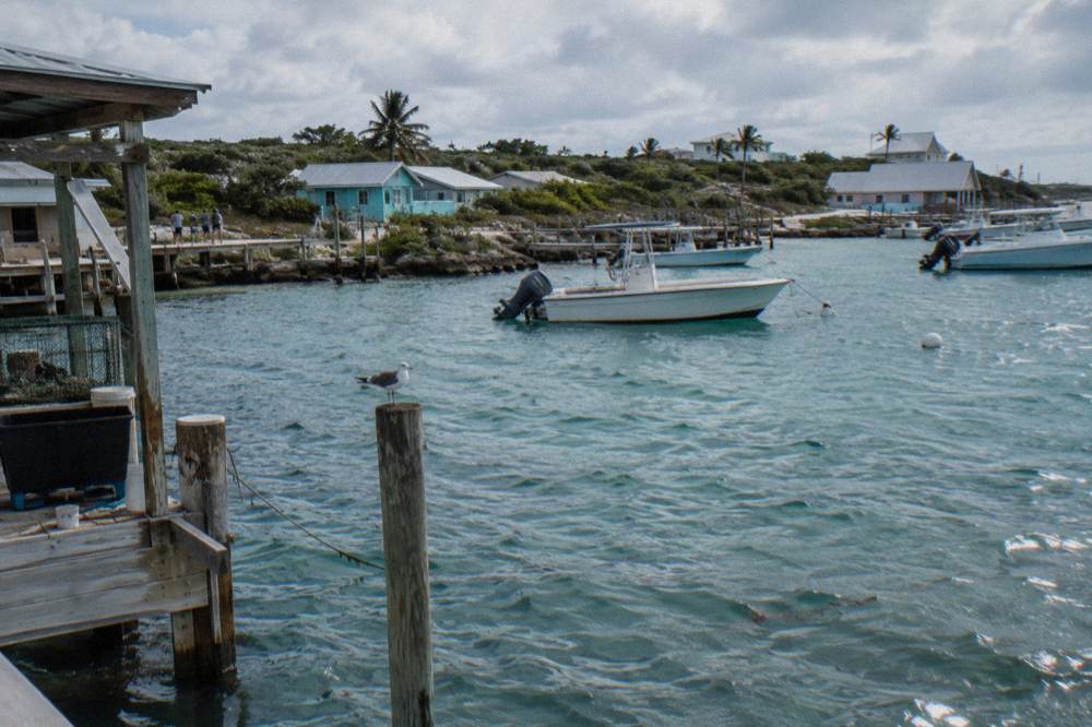A small cay with a cluster of dock roofs above clear water and moored boats at anchor