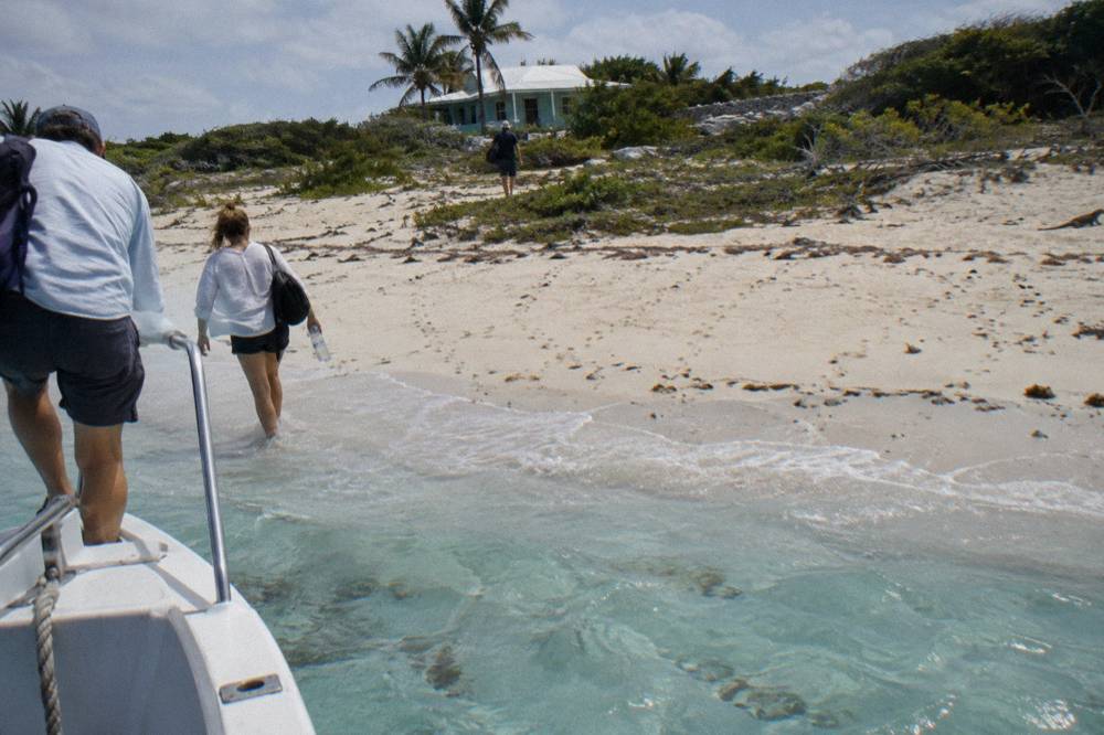 Boat passengers stepping onto a white sand beach at a small Exuma cay