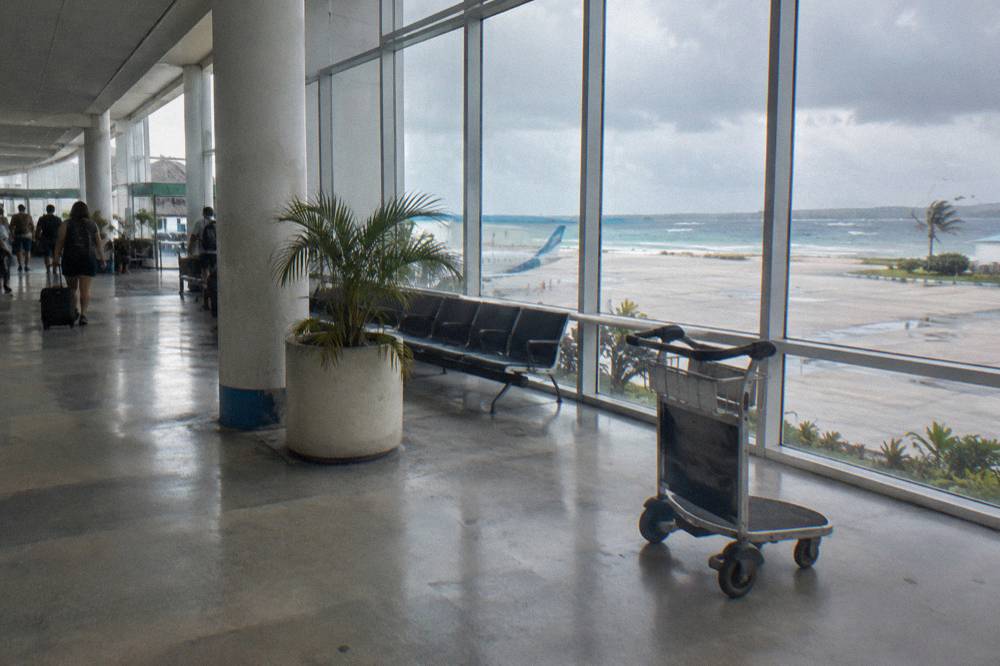 Airport departure board above a quiet terminal with travelers waiting at a gate