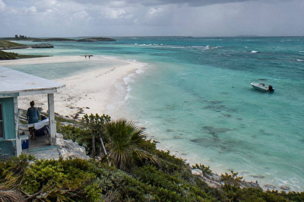 A white sandbar curving through clear shallow water with a small boat anchored nearby