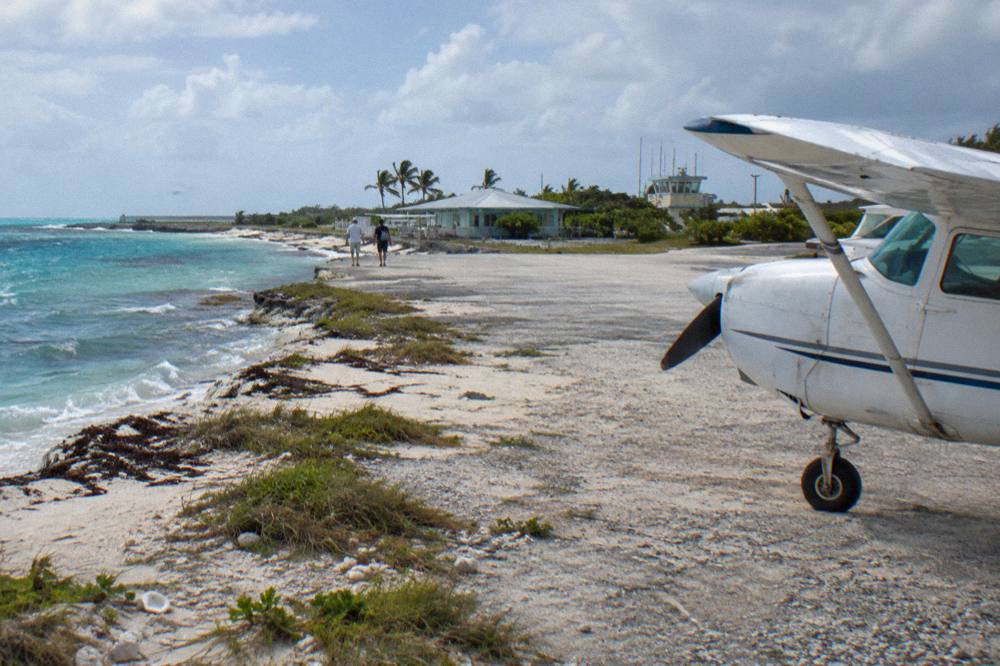 A light aircraft on a small grass airstrip beside turquoise water