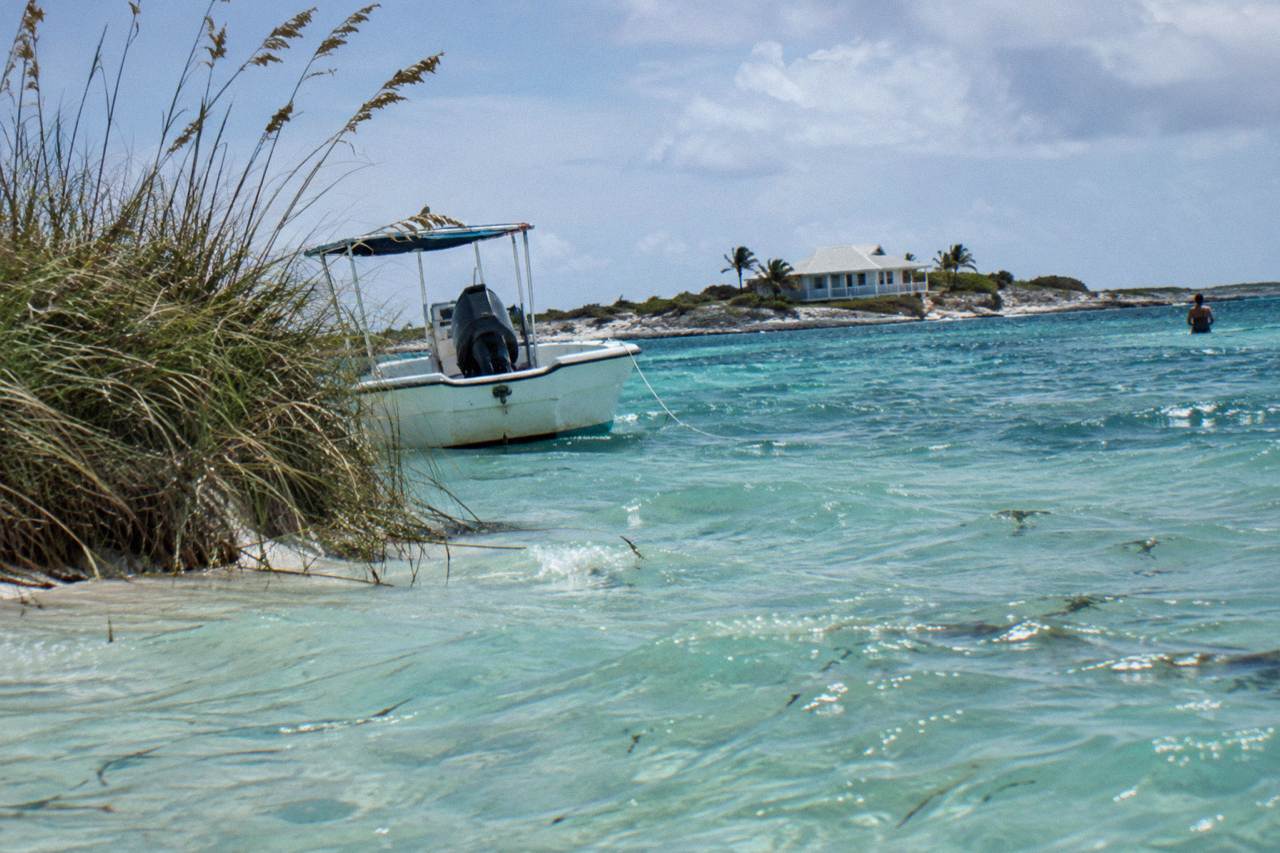 Turquoise shallow water around a small Exuma cay with a white sand beach and a moored boat