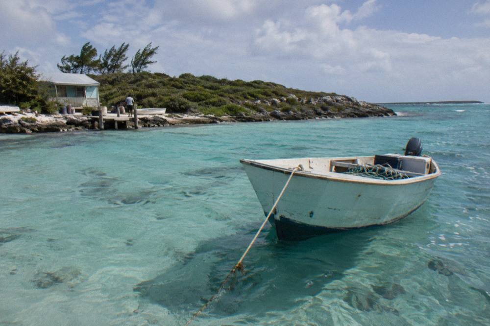 A boat anchored in clear turquoise water beside a small Exuma cay