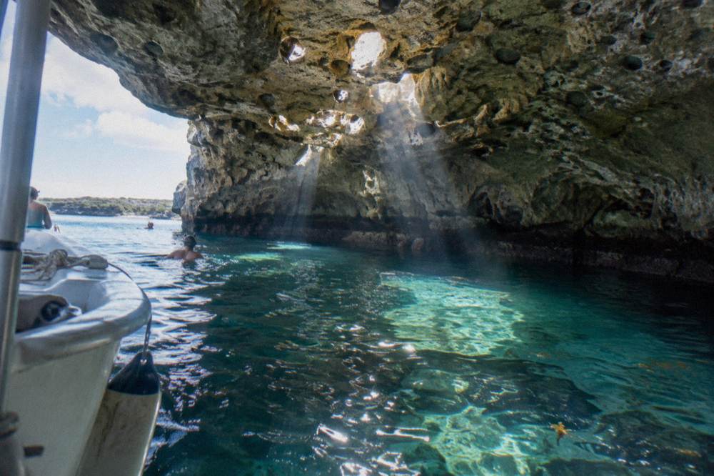 Sunlight streaming into a clear blue underwater cave opening over coral