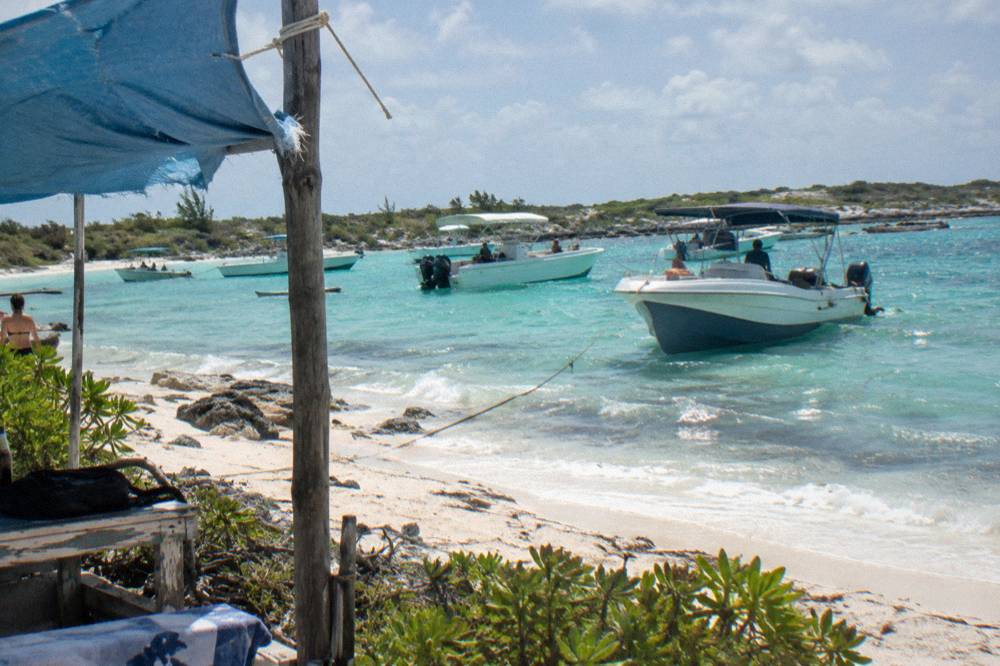 Several tour boats anchored in shallow turquoise water beside a small beach