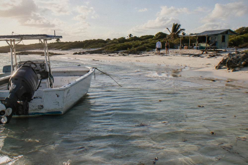 A boat resting in shallow water beside a strip of white sand