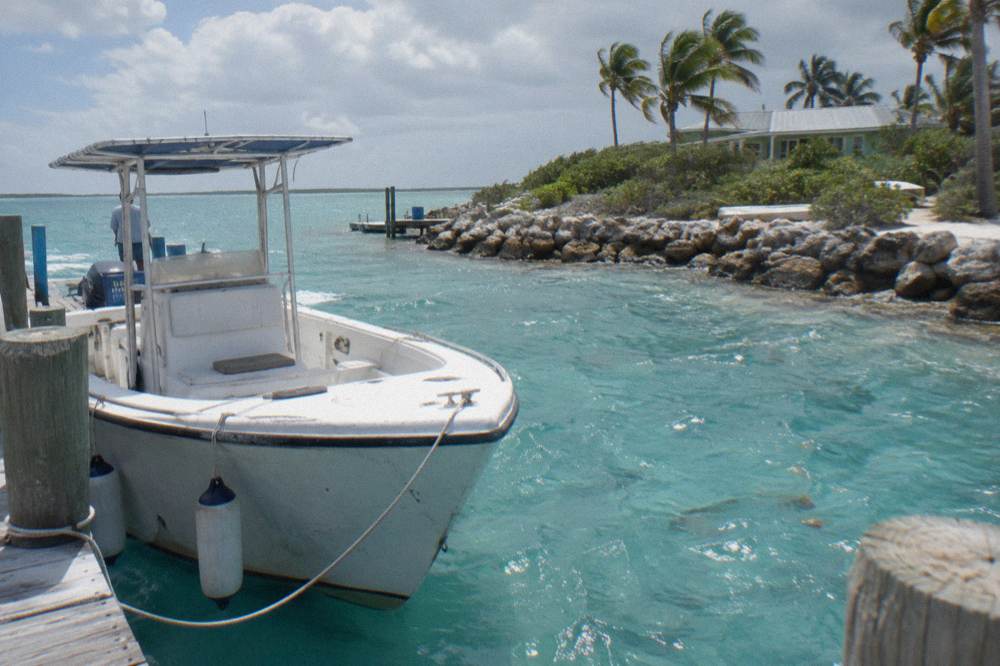 A white powerboat tied at a small marina dock surrounded by turquoise shallows