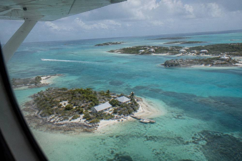 A light aircraft on approach over shallow turquoise water and scattered cays