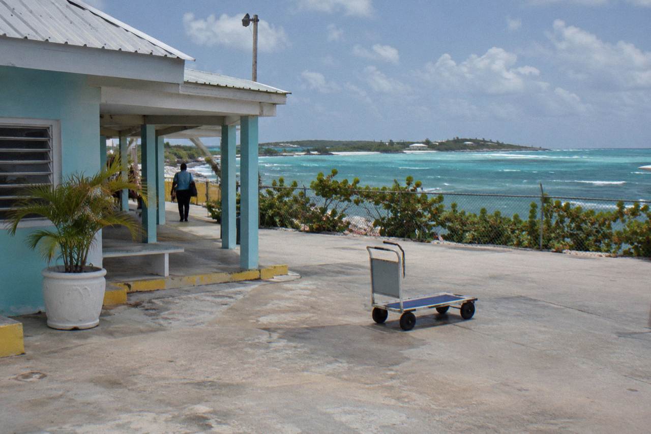 A small airport terminal building beside a turquoise bay under scattered clouds