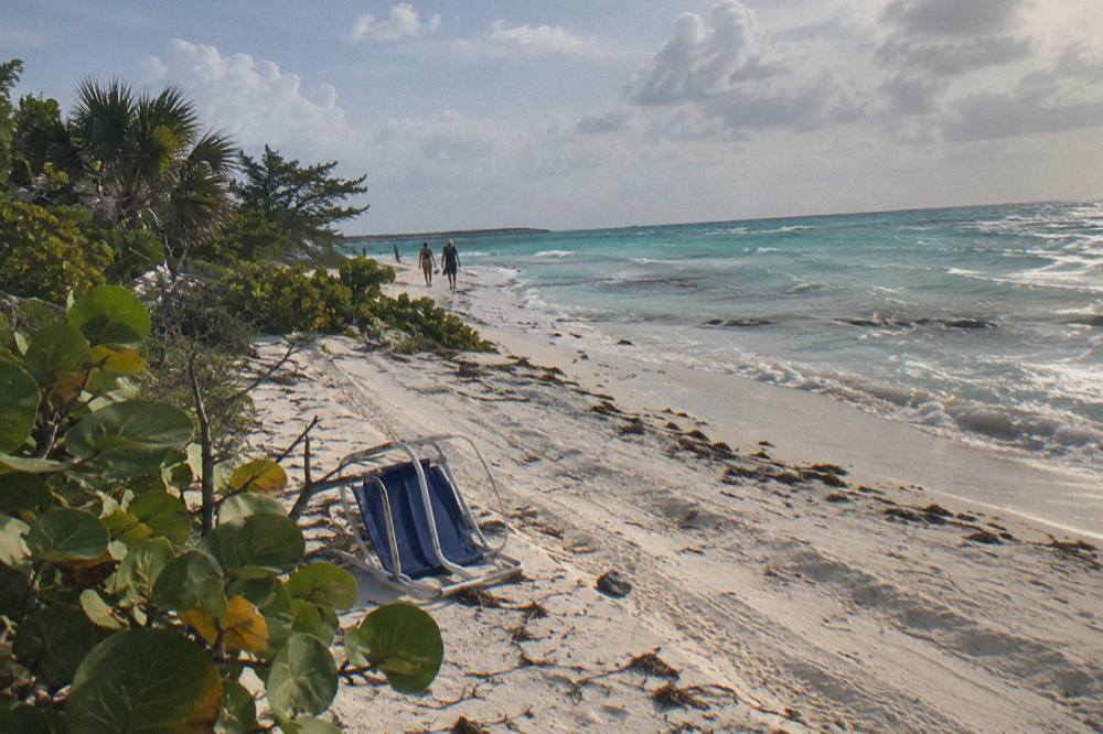 Wide pale sand beach with calm shallow turquoise water and scattered low vegetation