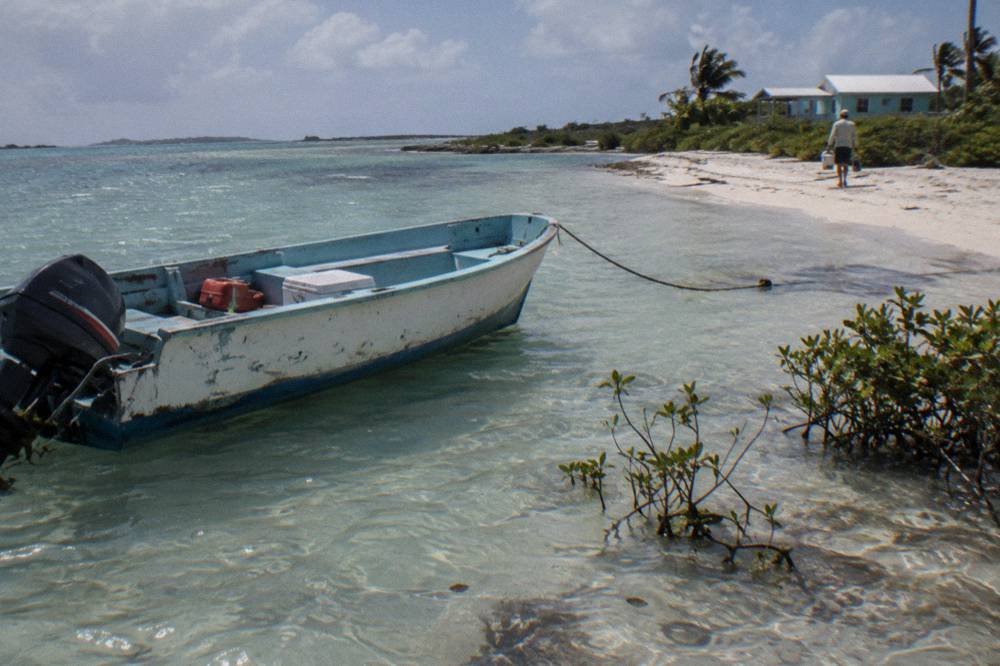 Boat anchored in shallow clear water beside a narrow strip of white sand