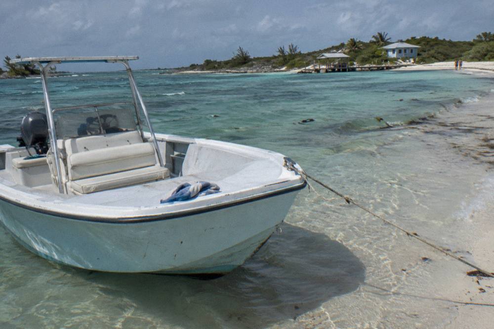 An open powerboat moored beside a white sandbar in clear shallow water