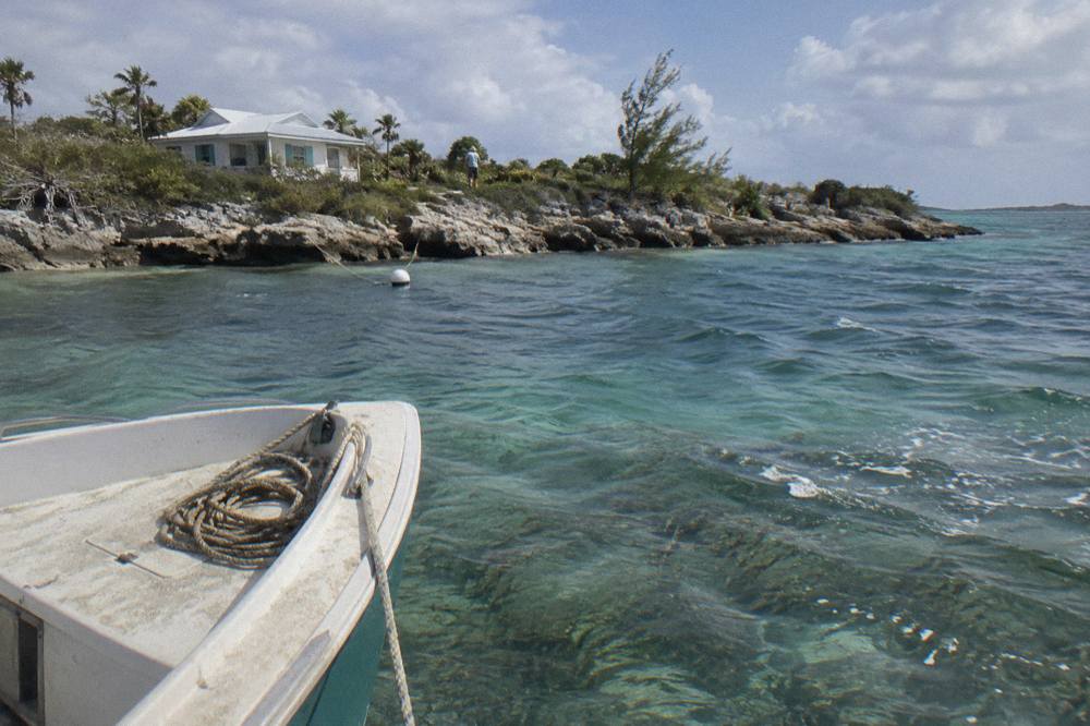 A narrow motorboat anchored in clear shallow water beside a small scrubby cay