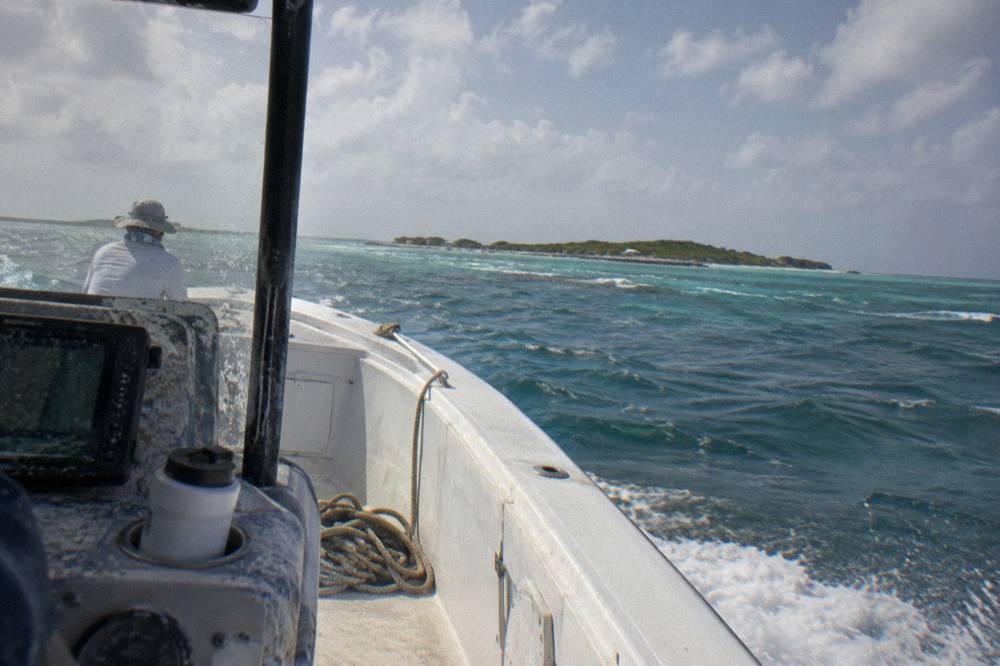 A speedboat cutting across open turquoise water toward distant low-lying cays