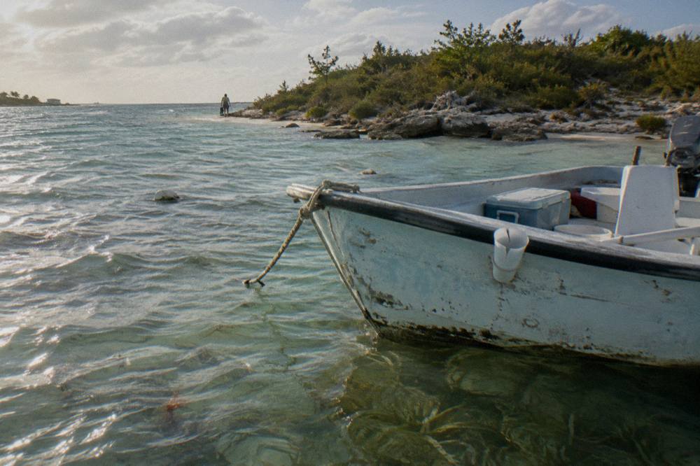 Small boat anchored in clear shallow water beside a white sand cay
