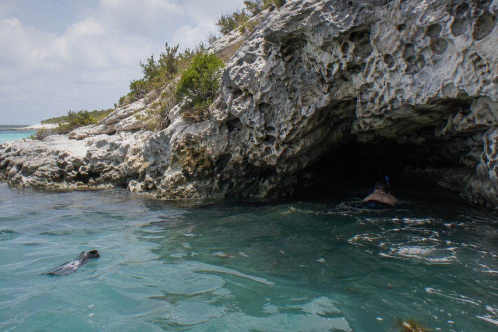 Snorkeler entering a small sea cave grotto from calm water