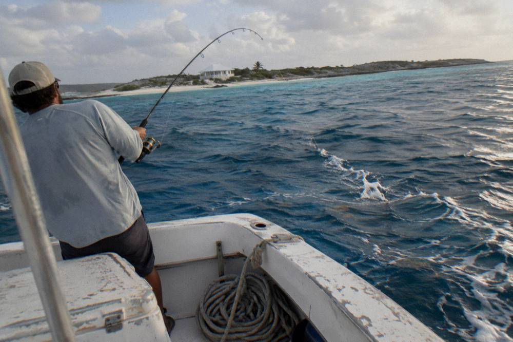 Angler reeling in a rod at the stern of a boat in clear blue water