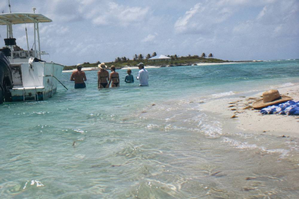A family standing in shallow water beside a boat at a quiet sandbar