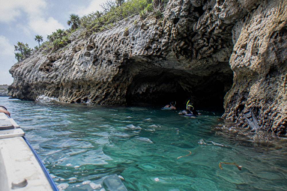 Snorkelers entering a limestone cave grotto from calm clear water