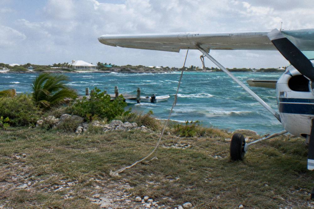 A small plane on a grass airstrip beside a blue cay harbor