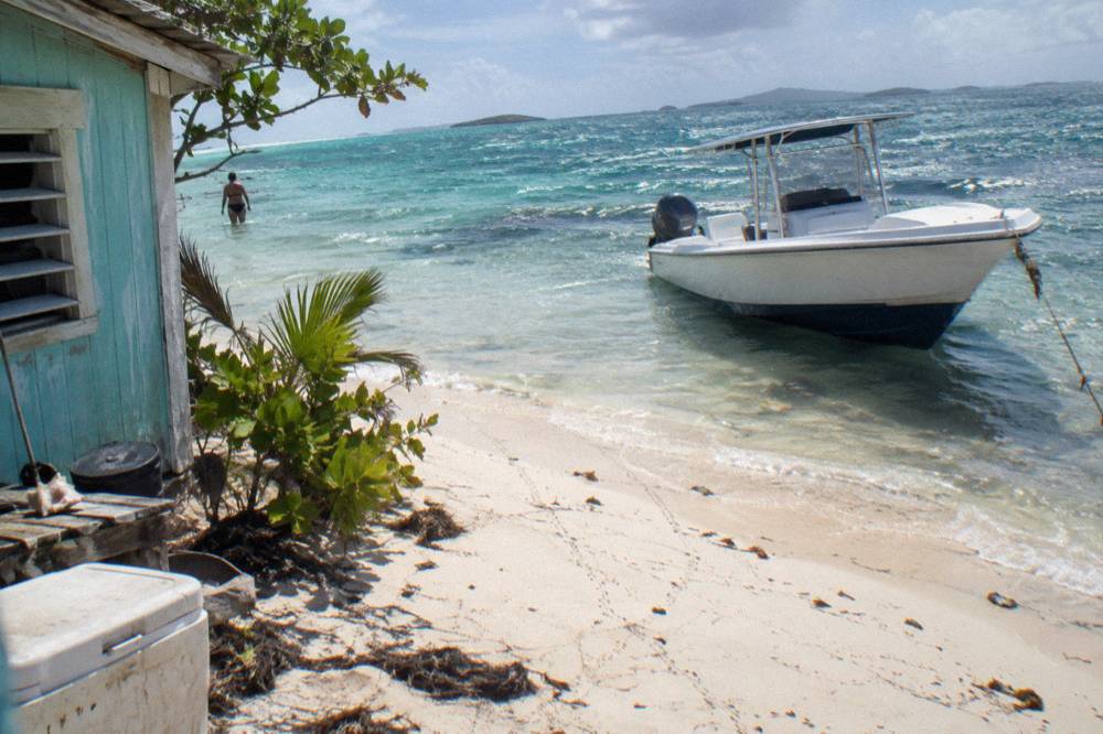 A speedboat anchored beside a strip of sand in clear shallow water