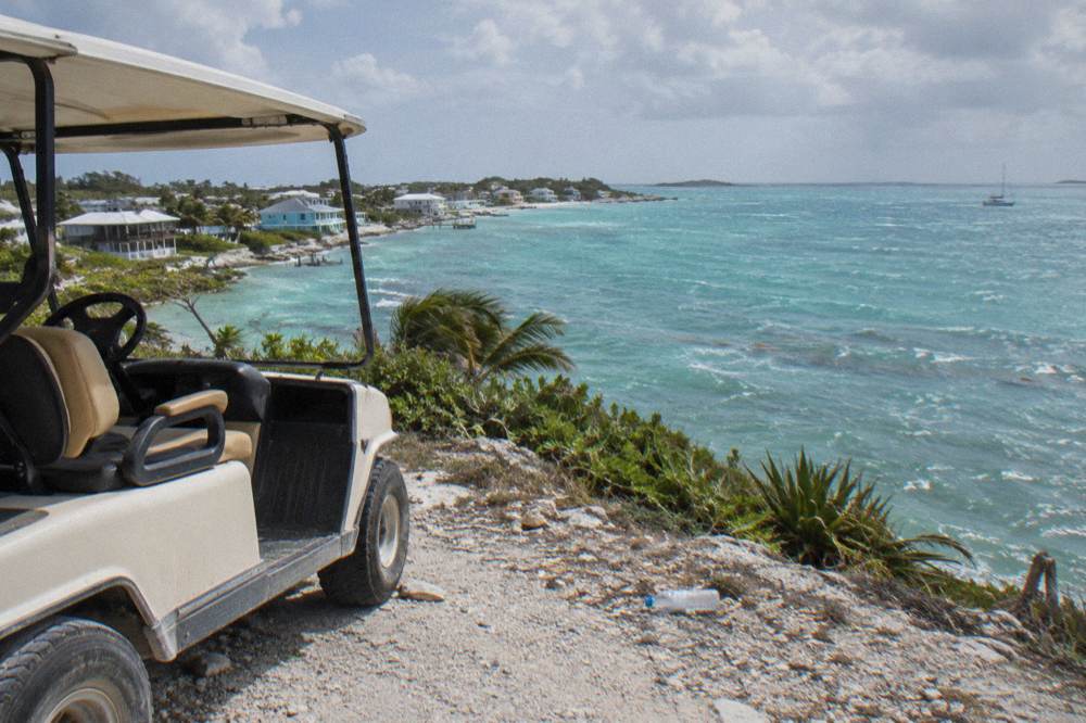 Open-sided buggy parked on a quiet coastal road beside calm turquoise water in Exuma