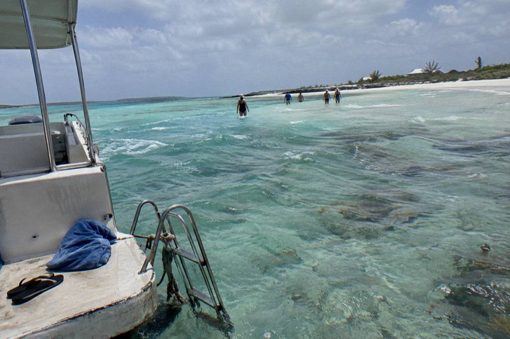 Tour boat anchored beside a shallow sandbar with guests wading in clear turquoise water among Exuma cays