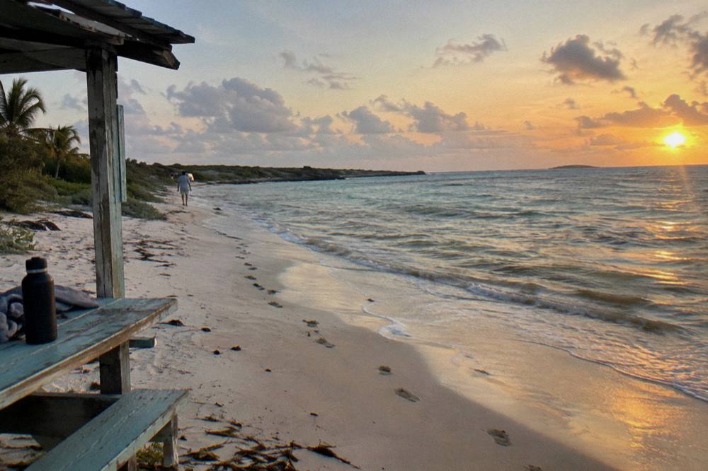 Wide empty beach at golden hour with soft light over calm shallow water and scattered clouds