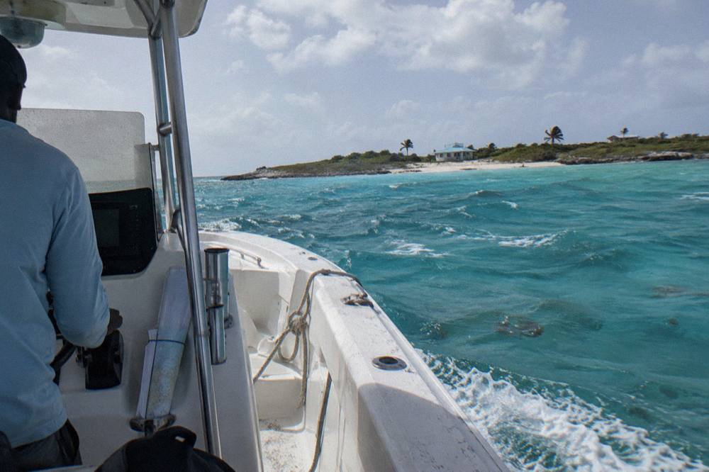 Speedboat cutting across clear turquoise water toward a small Exuma cay