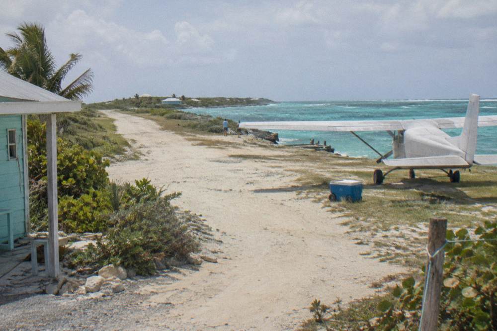 Small plane on a grass airstrip beside turquoise sea at a Bahamian cay