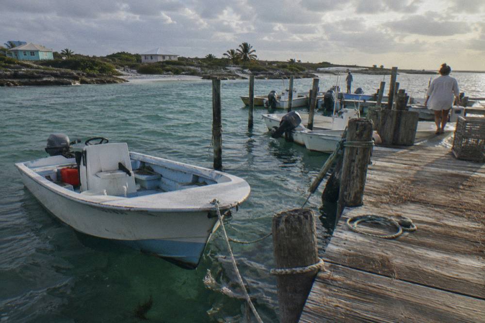 Wooden dock with small boats moored beside calm green water at a Bahamian cay