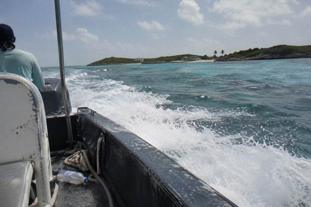 A speedboat planing across open water toward low Exuma cays