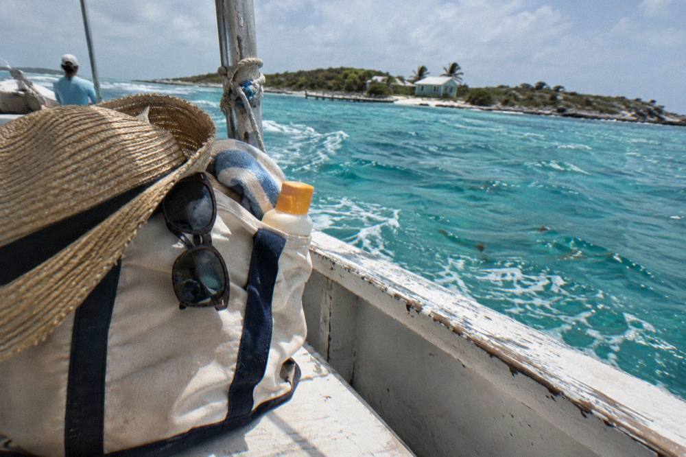 A packed beach bag with hat, sunglasses and reef-safe sunscreen beside a boat rail