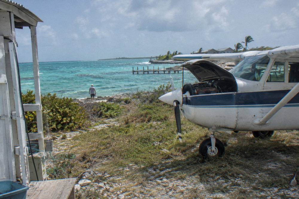 A small plane on a grass airstrip beside turquoise water at a Bahamian cay