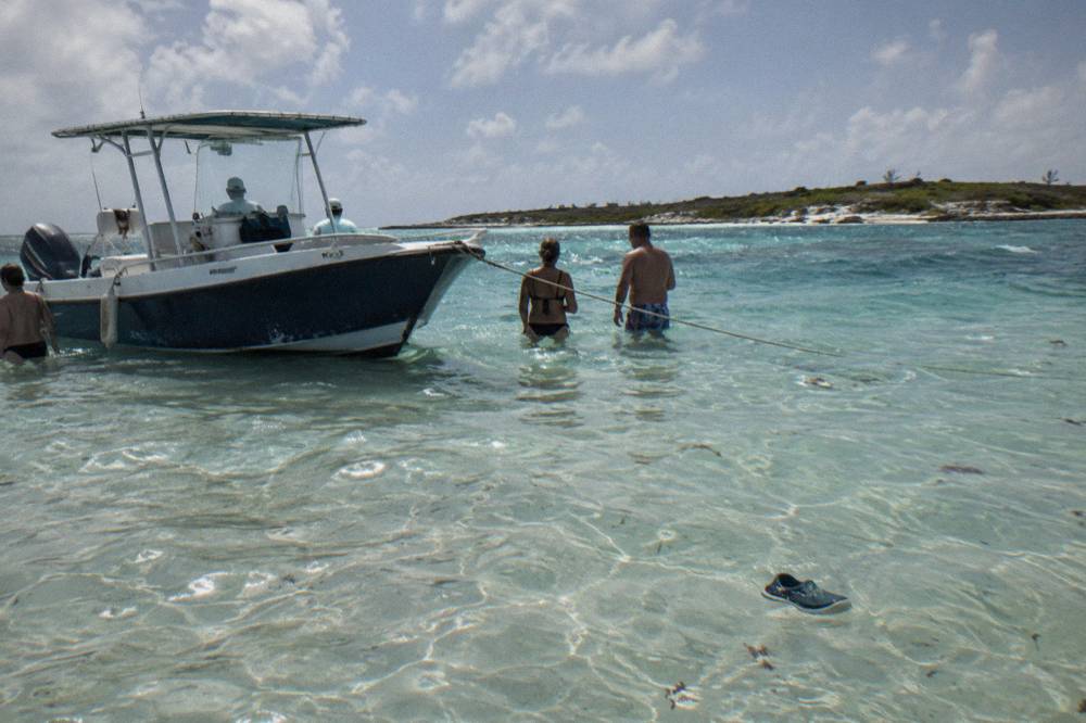 A covered powerboat anchored beside a sandbar with guests standing in waist-deep clear water