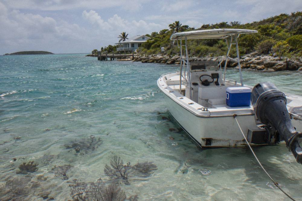A white powerboat anchored in clear shallow water beside a small Bahamian island