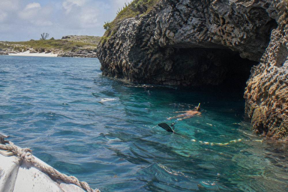Snorkeler swimming near a coral cave entrance in clear blue water
