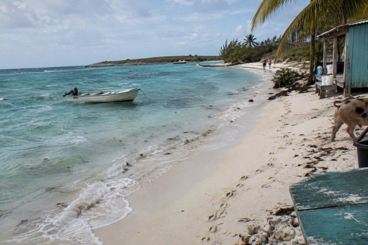 Turquoise shallow water at an empty Exuma beach with a small wooden dinghy moored offshore